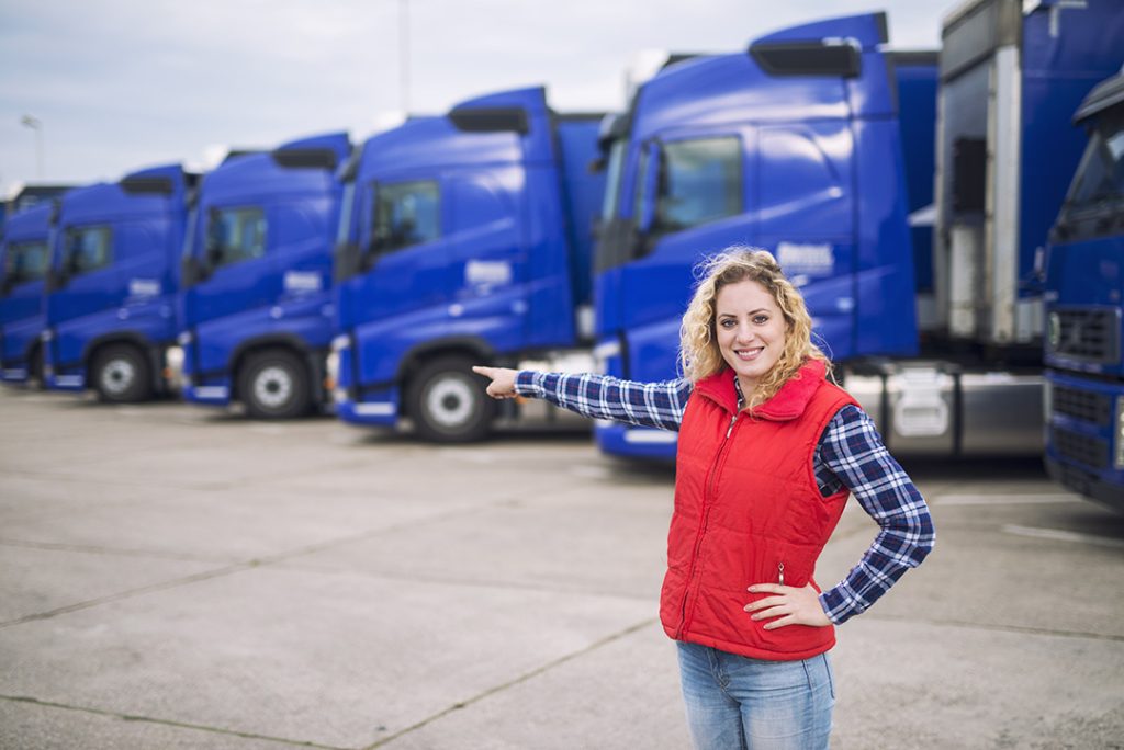 camionero-mujer-pie-frente-camiones-estacionados-apuntando-dedo-vehiculos-transporte
